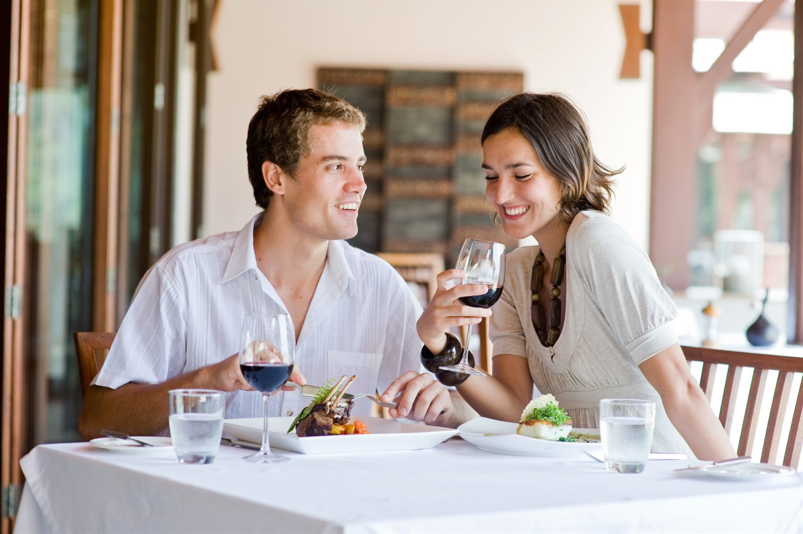 Couple smiling over glasses of red wine at a dinner table set with white linen